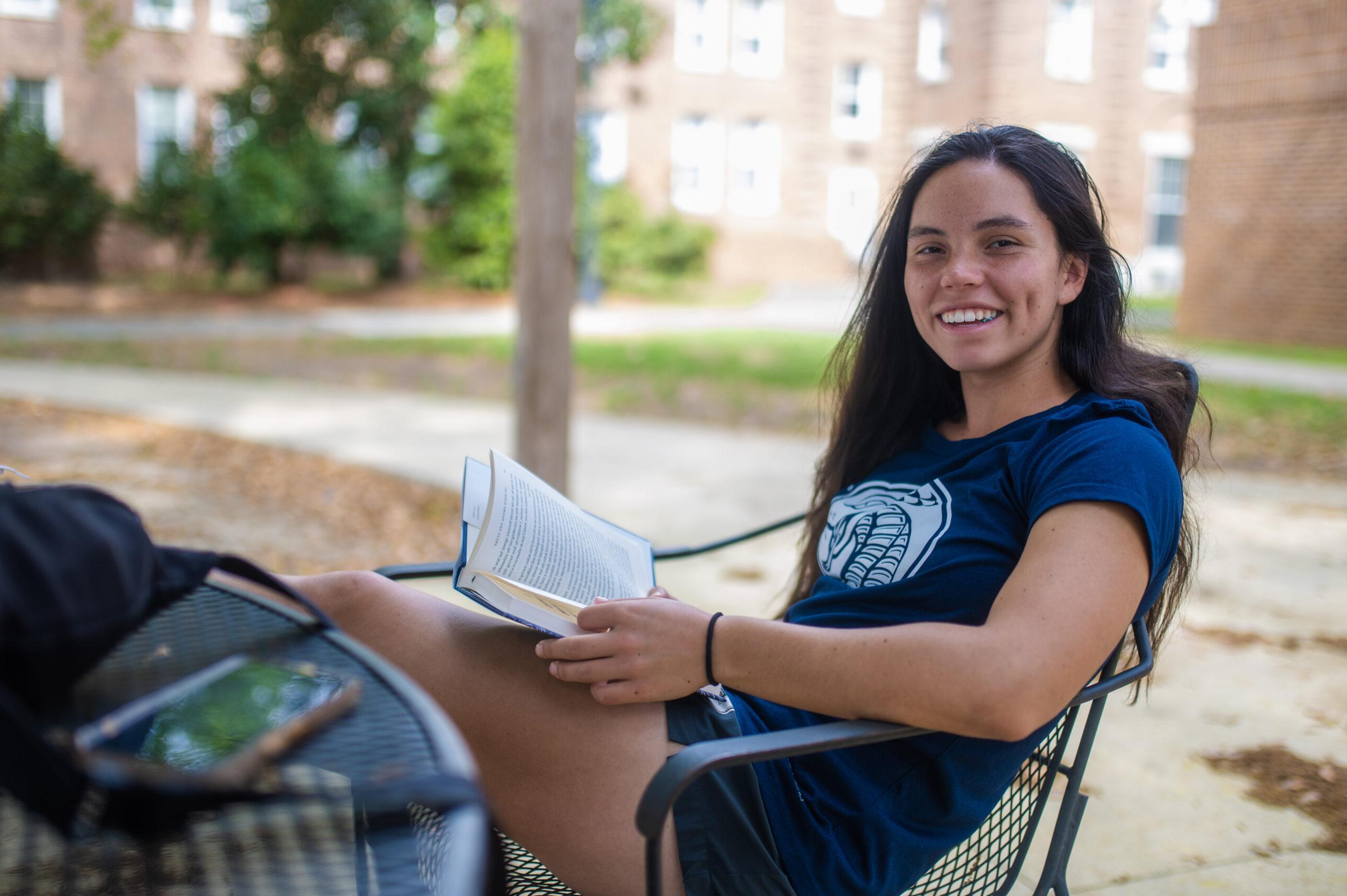 一个学生懒洋洋地坐在椅子上，手里拿着一本书，对着镜头微笑